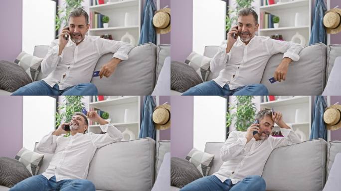 快乐的年轻西班牙人，白发苍苍，自信地用智能手机谈生意，手里拿着名片，坐在家里的沙发上放松。