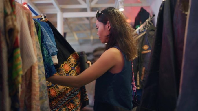 年轻的女游客在她的假期在旧货店看二手衣服