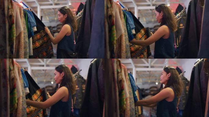 年轻的女游客在她的假期在旧货店看二手衣服