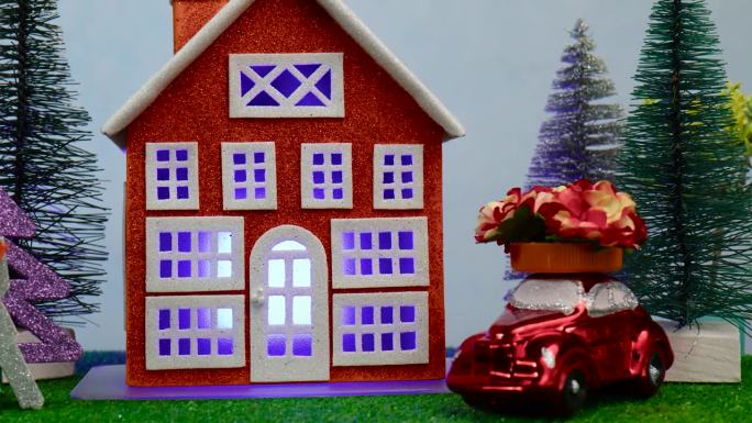房子附近的特写，有发光的窗户，一棵挂着钥匙的圣诞树和一辆车顶上有花的汽车