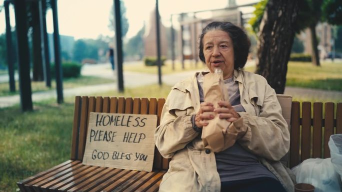 不整洁无家可归的老年妇女喝酒，在公园长椅上乞讨，穷困潦倒