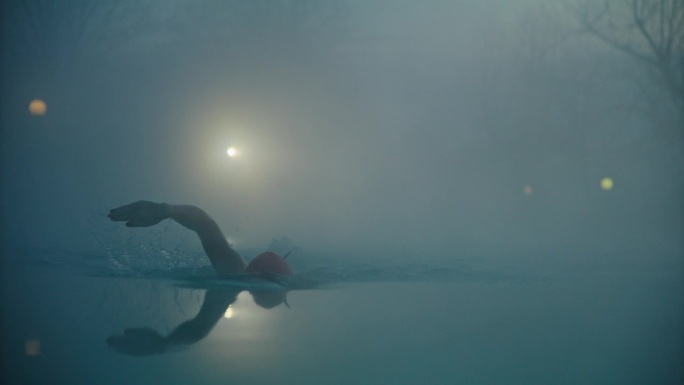 在清晨大雾天气中，坚定的女游泳运动员在泳池里练习自由泳的镜头