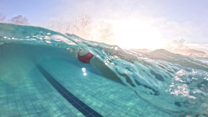 白天在旅游胜地游泳池游泳的坚定女子的部分水下跟踪拍摄