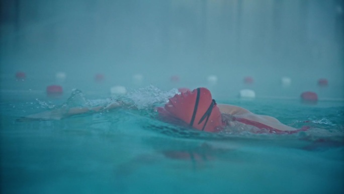 运动的年轻女子戴着帽子和护目镜在旅游胜地的游泳池游泳的镜头