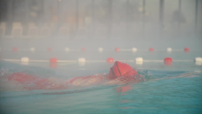 在晴朗的雾天里，坚定的年轻女子在泳池里练习自由泳