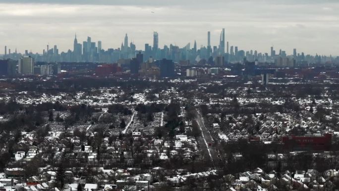 下雪后郊区的鸟瞰图。纽约的天际线可以在地平线上看到，阴天的时候地面上有雪。无人机摄像机，在卡车左侧的