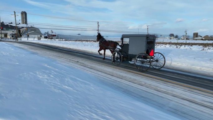 空中跟踪拍摄的马车在阿米什国家与雪在冬天。马和马车的空中轨道拍摄。