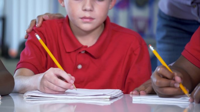 小男孩在课堂上写字，老师帮助