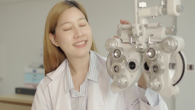 迷人的年轻女医生双臂交叉站在验光设备附近，检查病人的眼睛视觉系统，眼镜店，眼镜店。启动新业务，小型业