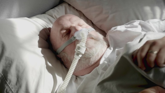 成年男子在被诊断为睡眠呼吸暂停并戴着睡眠面罩后，用CPAP(持续气道正压通气)机睡觉