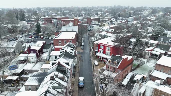 美国城市在小雪期间。鸟瞰图，一条白雪覆盖的街道两旁排列着汽车和红砖房屋。
