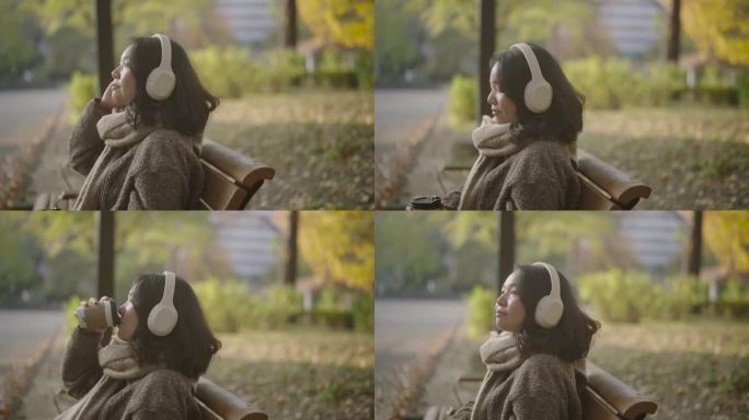 一个寒冷的秋天，年轻的亚洲女子在公园里放松。她用智能手机戴着耳机听音乐。