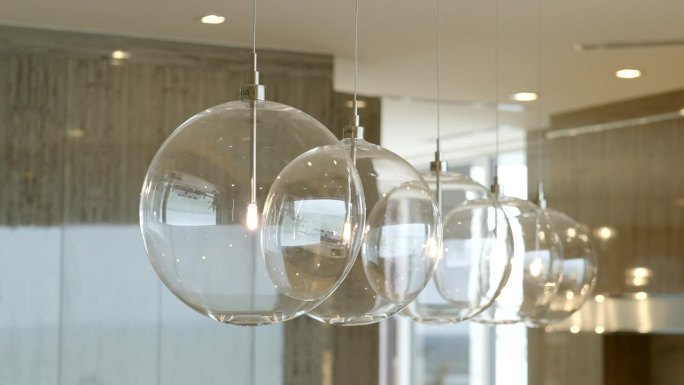 在现代设计公寓的模糊背景下，透明的圆形灯泡以球的形式悬挂在悬挂的天花板上，以温暖的阴影闪电排列