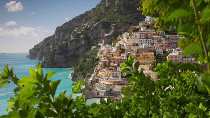 意大利阿马尔菲海岸美丽的波西塔诺村。镜头在绿叶之间移动，俯瞰波西塔诺村绿松石水的海滩，五颜六色的房子