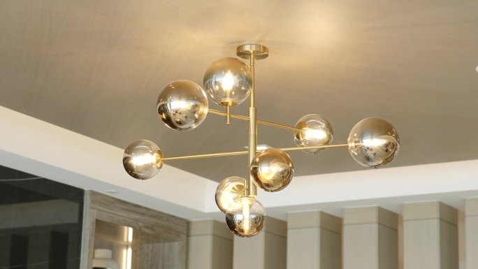 抽象的现代吊灯，圆形灯由金色金属辐条连接，悬挂在白色石膏踢脚板的吊顶上