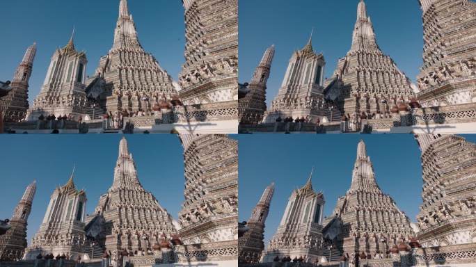 在晴朗的蓝天下，泰国传统寺庙的精致塔尖，游客们探索着华丽的建筑细节