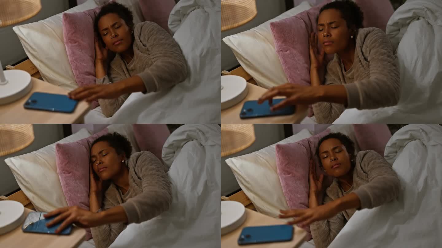 一个卷发的成年女人在床上显得很不安，在夜间的卧室场景中，她伸手去拿手机。