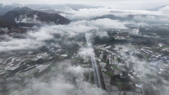 俯瞰春天云雾缭绕下贯穿山间田野的高速公路