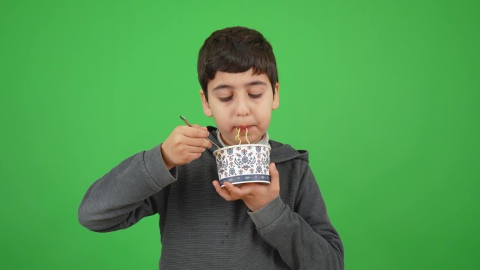 一个八岁的小男孩端着一碗面，开心地吃着