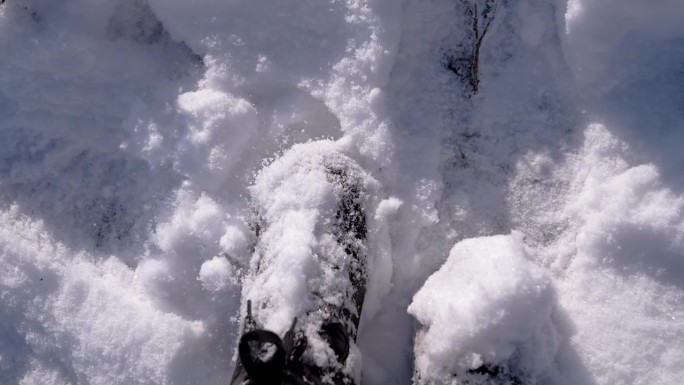 俯视图女子在雪中站在雪堆上，抖掉黑色靴子上的雪