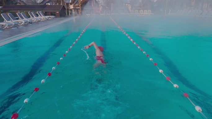 在户外度假胜地雾蒙蒙的游泳池里练习自由泳的坚定的年轻女子的后景跟踪镜头