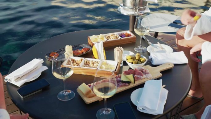 一群人在泳池边享用开胃酒，朋友们坐在桌子旁品尝美味的传统意大利开胃酒，高脚杯里有清爽的白葡萄酒，意大