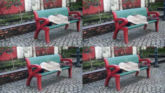 印度北阿坎德邦德拉敦市，无家可归的人盖着毯子睡在公园长椅上。城市无家可归者和脆弱性的真实写照