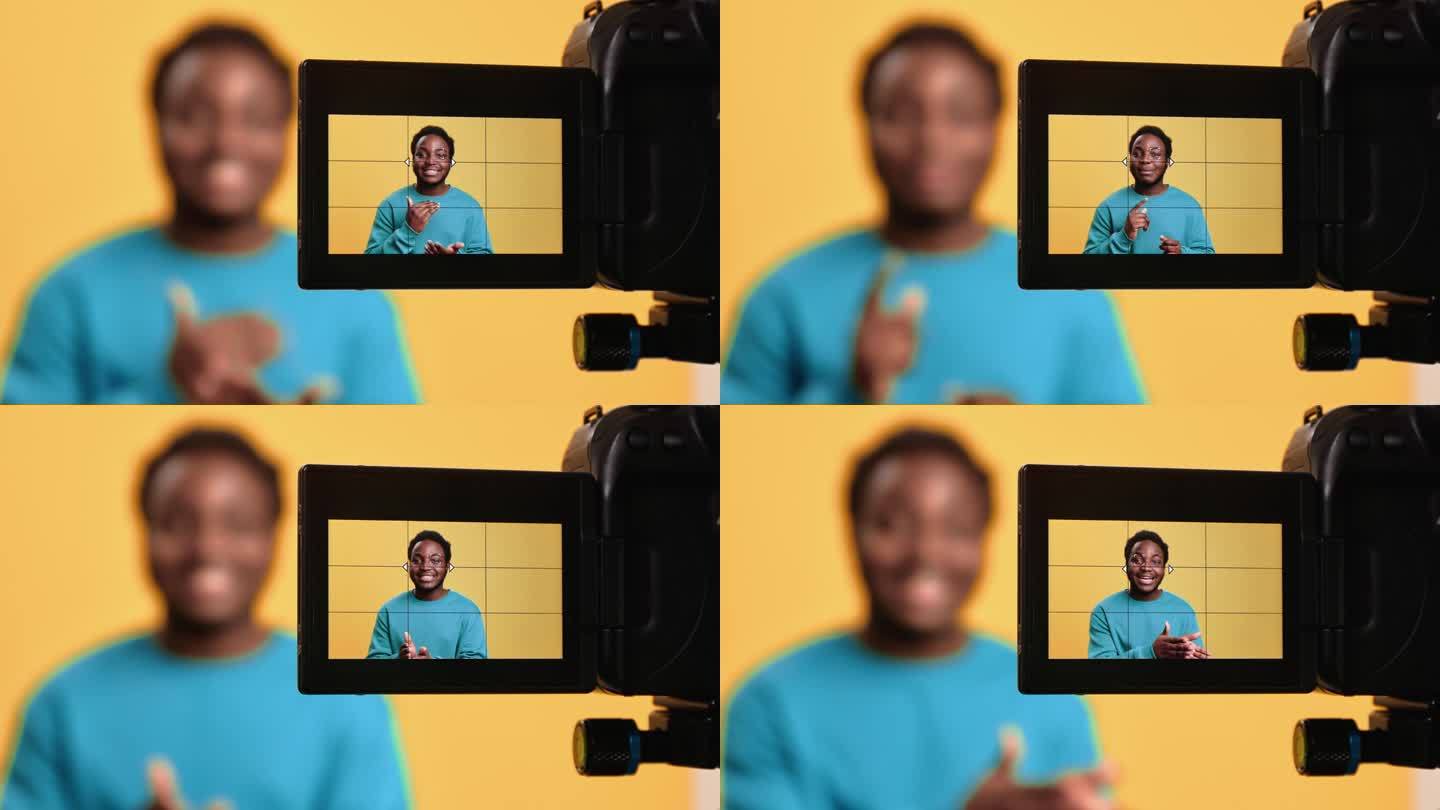 微笑的非洲男人网红拍摄视频博客视频博客摄像机屏幕上的橙色工作室独自摆姿势