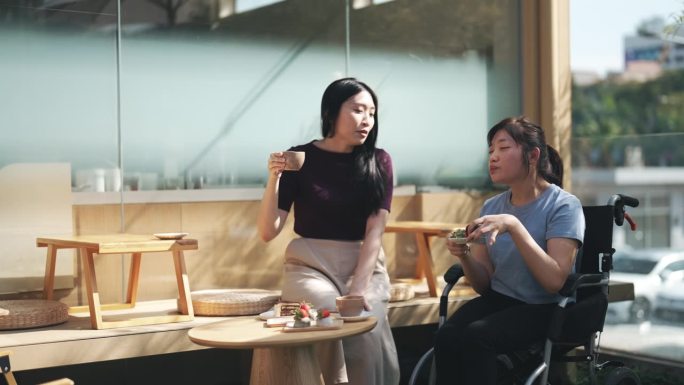 周末早上，快乐的亚洲华人脑瘫妇女坐在轮椅上和朋友在日本咖啡馆前
