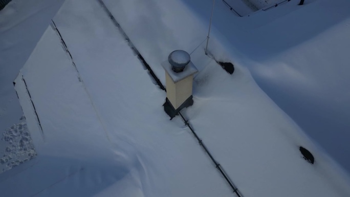 冒烟的烟囱，还有一个屏障在积雪的屋顶上，以防止雪滑下来。金属棒固定层。用无人机检查烟囱里的烟气将拯救