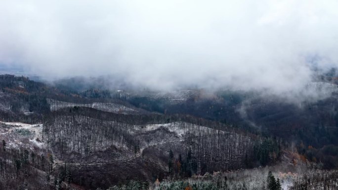 无人机在多雪的山区上空飞行，云层断断续续地遮住了下面结霜的地面。