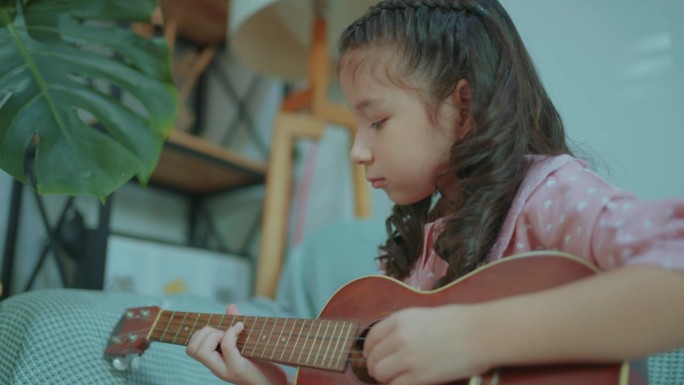 可爱的亚洲小女孩在客厅里弹着尤克里里，唱歌。