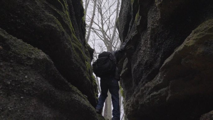 徒步旅行者通过压住岩石壁，把自己降到覆盖着树叶的森林地面上，爬下岩石裂缝