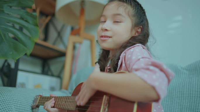可爱的亚洲小女孩在客厅里弹着尤克里里，唱歌。