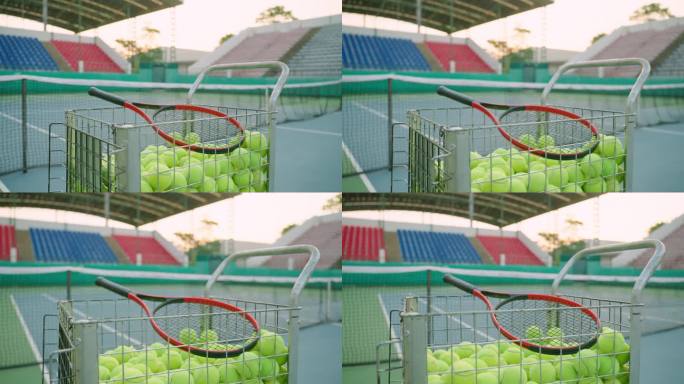 网球场的近景，一辆车载着许多绿色的网球，网旁边有一个练习用的球拍。