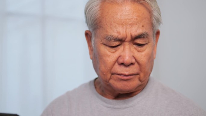 亚洲老人揉着眼睛，厌倦了长时间的凝视。一位老人因长时间盯着平板电脑而眼睛疲劳。
