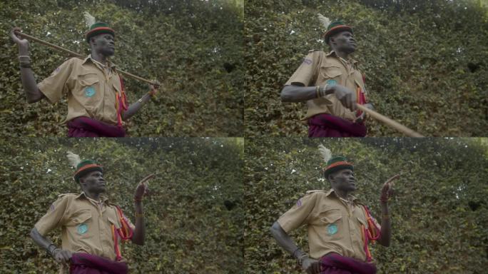 乌干达卡拉莫琼部落的非洲战士穿着制服，手持木棒，在户外用手指着。低角度拍摄