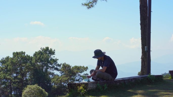 数字游牧民和旅行的概念与单独的自由职业者男人坐在木头和使用平板电脑工作从户外层山的背景