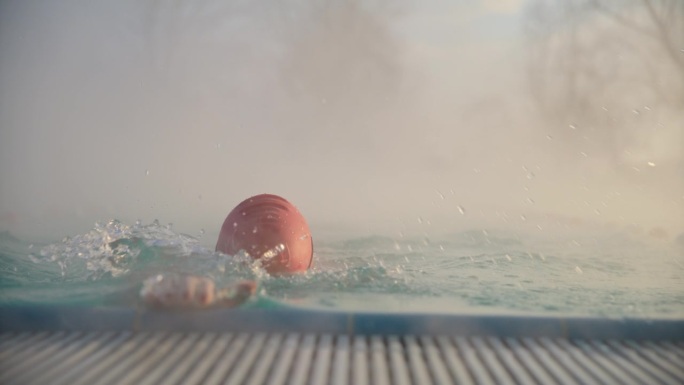 黎明时分，美丽的年轻女子在旅游胜地雾气覆盖的游泳池里游泳