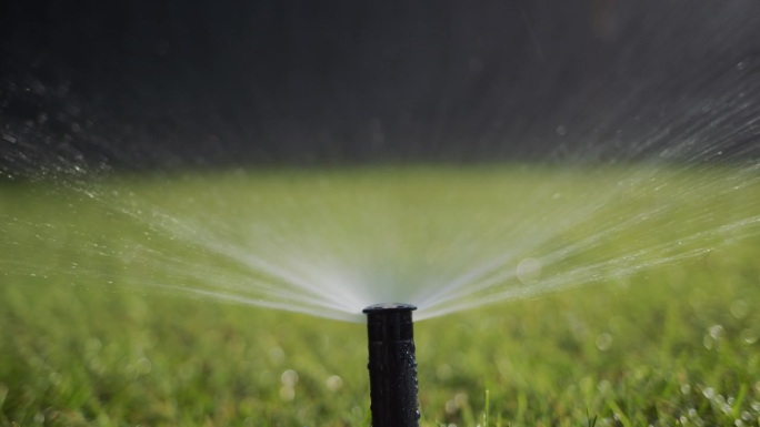 一股水流在压力下灌溉着绿色的草坪。滑块4k镜头