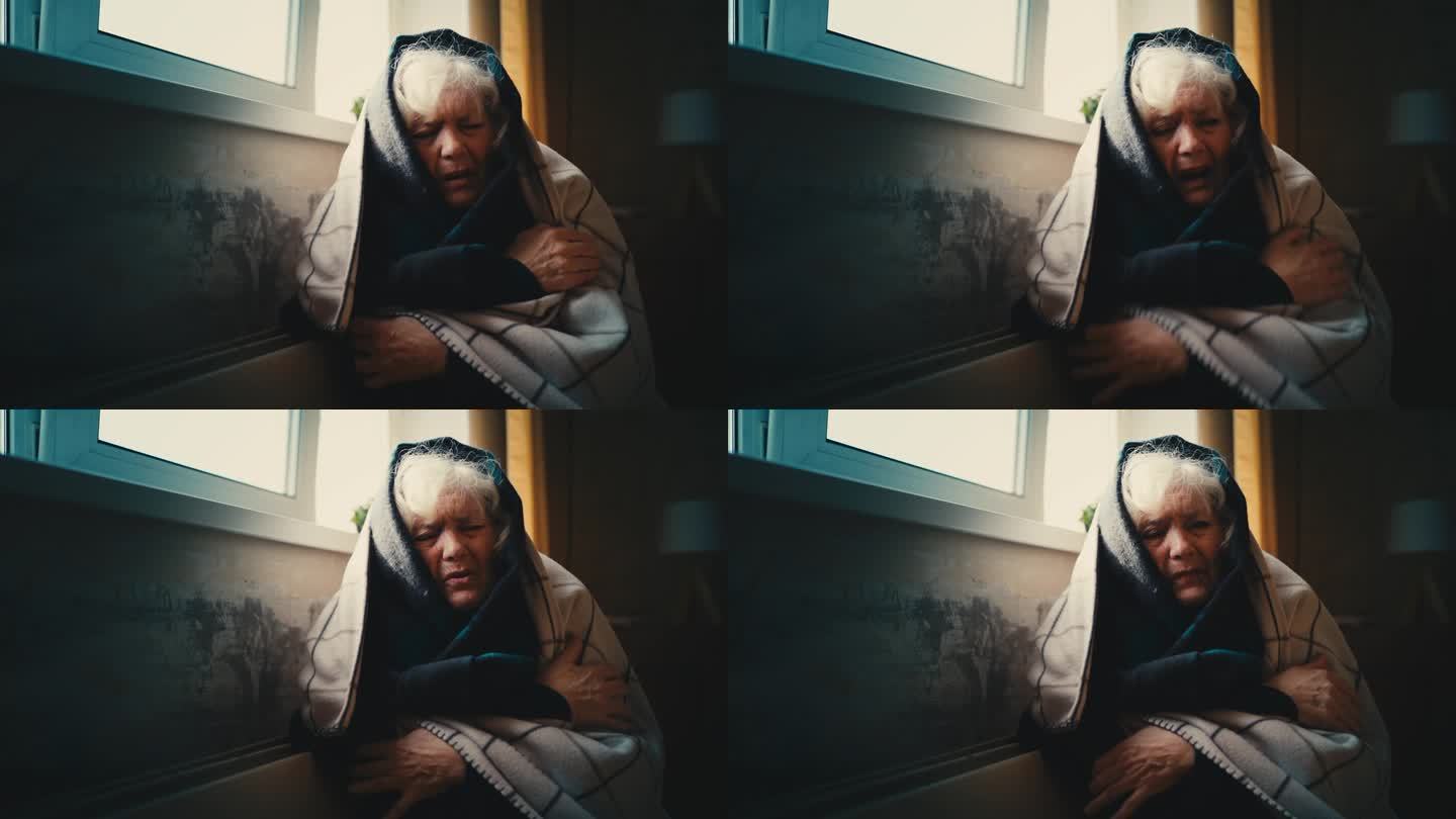 被冻僵的老年妇女裹在毯子里，试图在电热器旁取暖