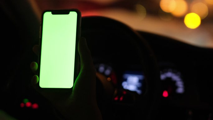 绿屏的手机在夜晚的汽车车内驾驶室里