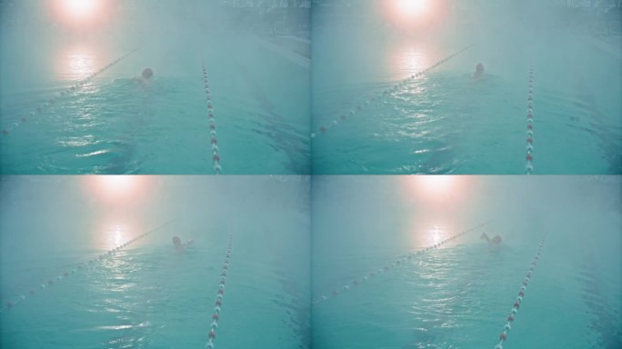 黎明时分，在旅游胜地雾蒙蒙的游泳池里练习自由泳的坚定女子的高角度后视图