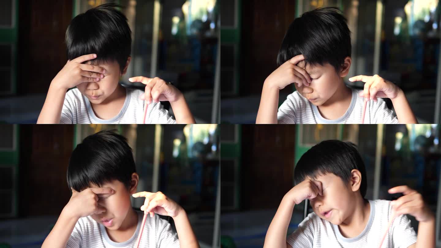 亚洲男孩在家里做家庭作业时感到困倦和疲倦，揉眼睛，打呵欠，脸上带着疲惫和厌烦的表情。不快乐的小孩概念
