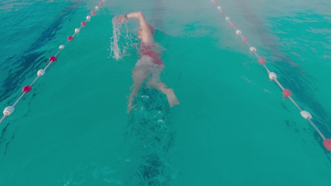 在度假村游泳池游泳的坚定运动女子的高角度后视图跟踪拍摄