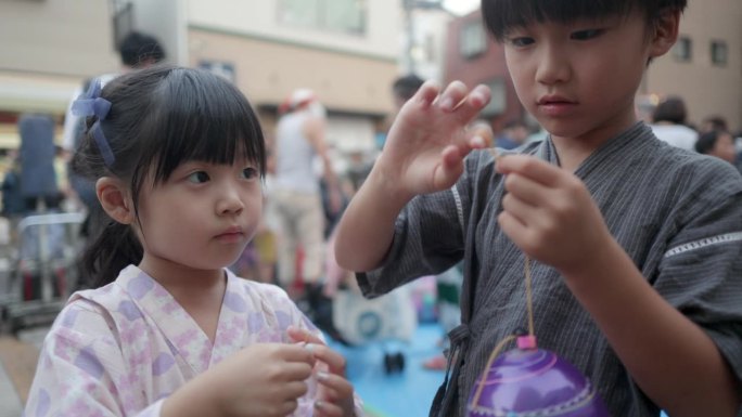 小妹妹和弟弟穿着浴衣在夏天的祭祭上玩水球悠悠球