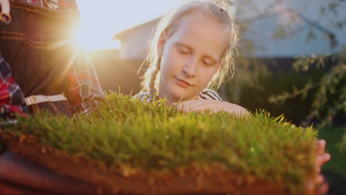 女孩抚摸着嫩绿的小草，一片长满小草的土地被农夫捧在手里。