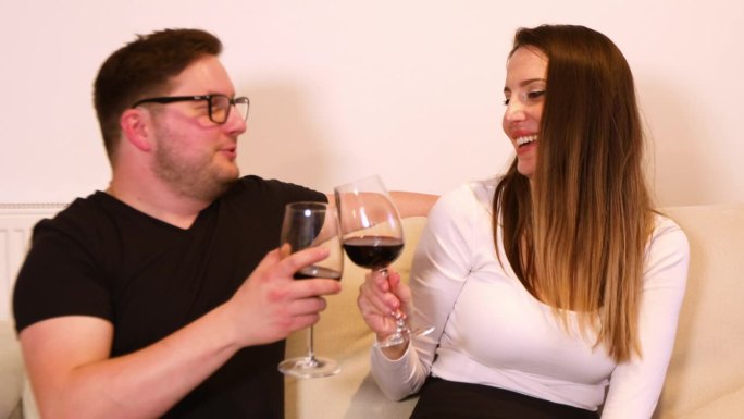 一对年轻夫妇坐在家里的沙发上，喝着红酒，谈笑风生的浪漫场景