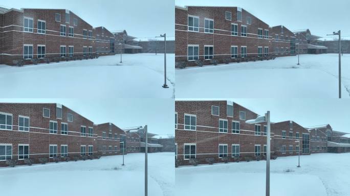 积雪覆盖的美式砖砌校舍，有大窗户。暴风雪中大型高中的航拍图。