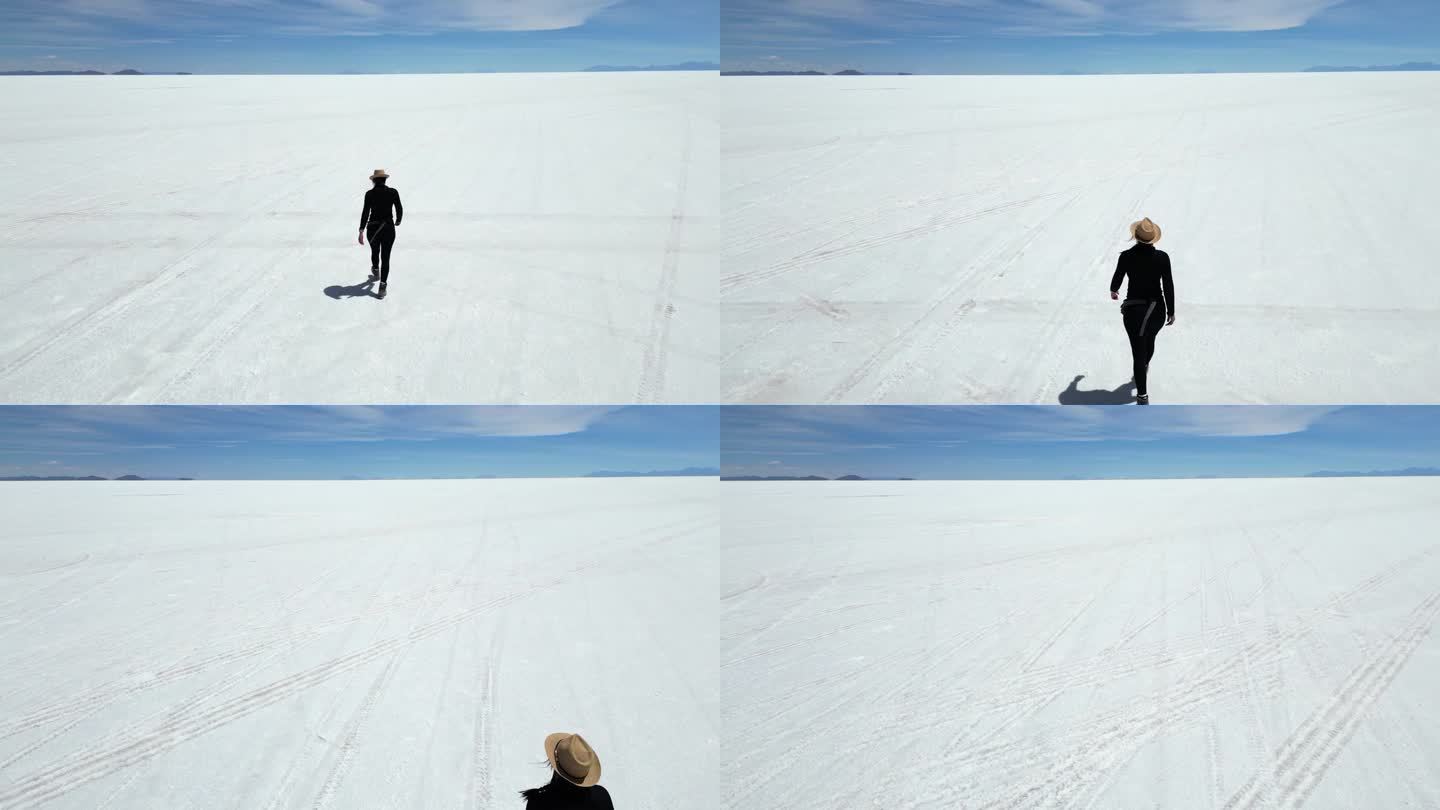 航拍画面显示，一名女子正朝着乌尤尼盐滩平坦的地平线走去
